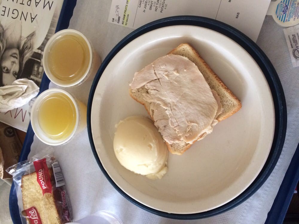 A hospital meal featuring bread with butter, mashed potatoes with gravy, and two cups of juice.