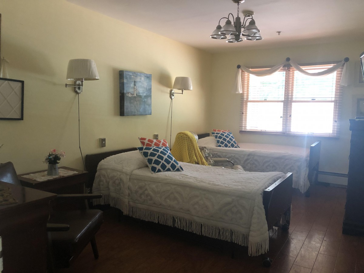 A cozy bedroom with two twin beds, elegant lighting, and a window letting in natural light.