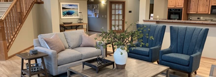 A cozy living room featuring a gray sofa, a blue armchair, and a large potted plant on a wooden coffee table.