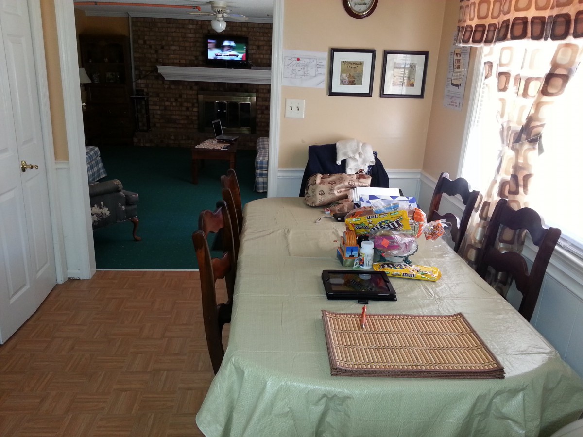 A dining area with a table covered in various items, connected to a living space.
