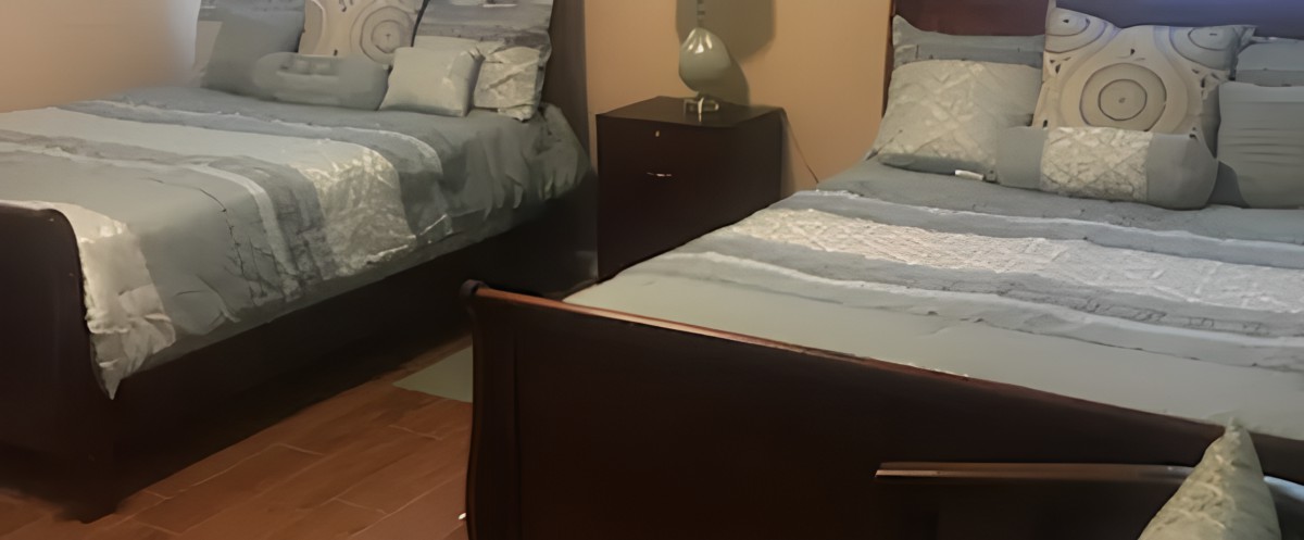 A cozy bedroom featuring two neatly made beds with a nightstand and lamp in between.