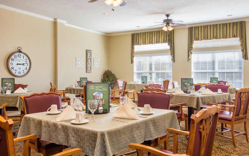 A cozy dining room with neatly set tables and wooden chairs, featuring soft lighting and elegant decor.