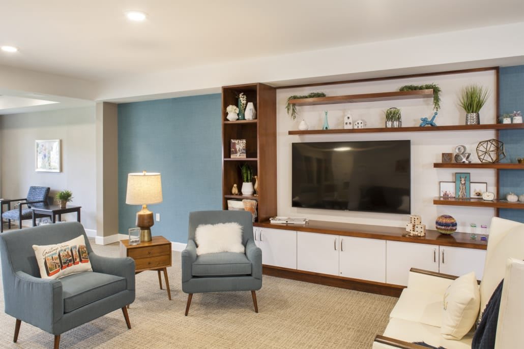 A modern living room with a TV unit, bookshelves, and comfortable armchairs.