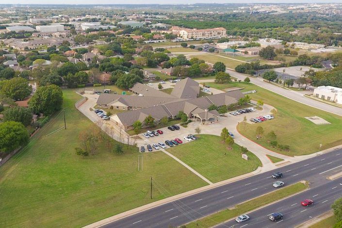 Aerial view of a suburban area with a large building complex and surrounding green spaces.