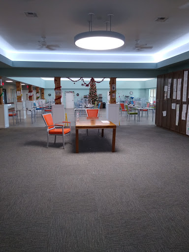 A modern lounge area featuring a table and two orange chairs, illuminated by soft overhead lighting.
