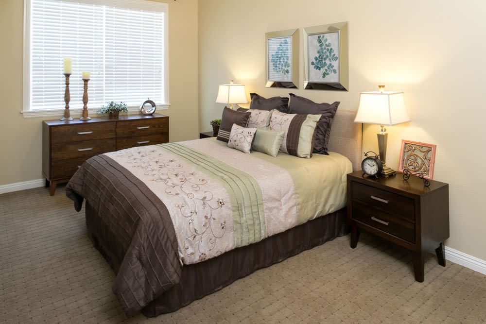 A cozy bedroom interior featuring a neatly made bed with decorative pillows, bedside lamps, and framed artwork on the wall.
