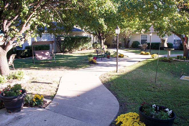 A serene garden path with benches and blooming flowers under the shade of trees.