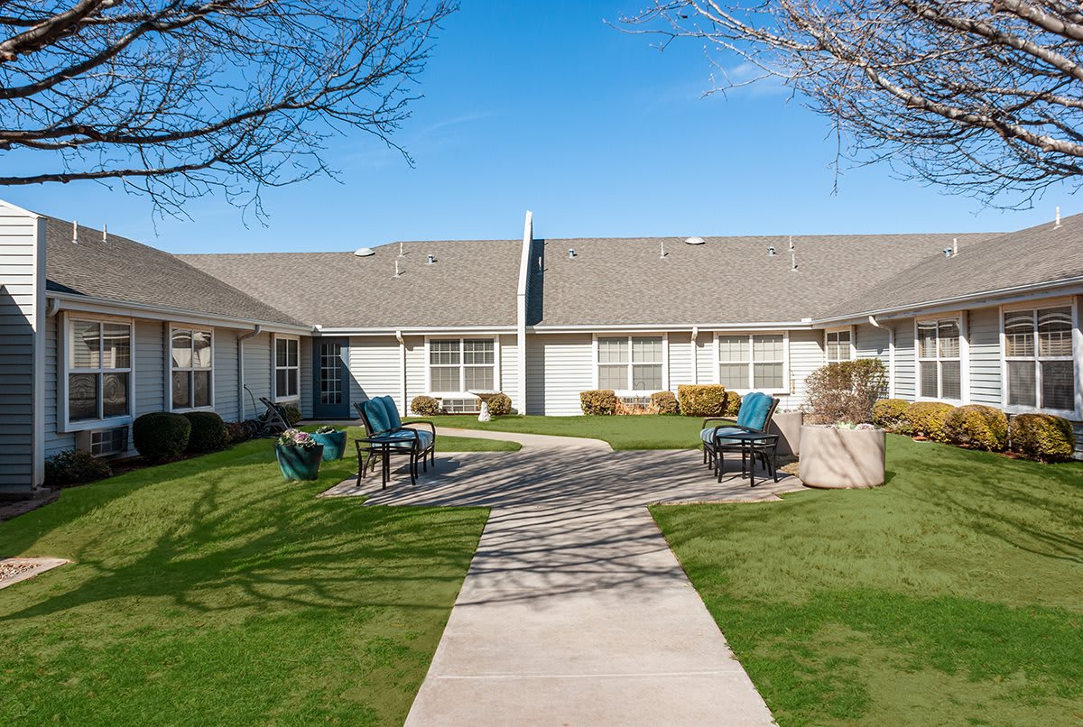 A residential area with a pathway leading to a house, surrounded by well-maintained lawns and outdoor seating.