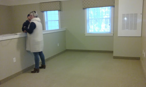 A person stands in an empty room with two windows, showcasing minimal furnishings.