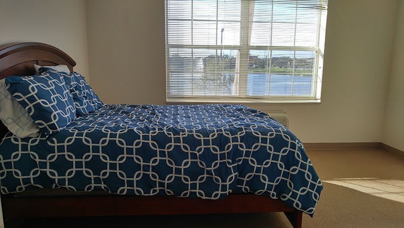 A bedroom with a blue-patterned bedspread and large window overlooking a scenic view.