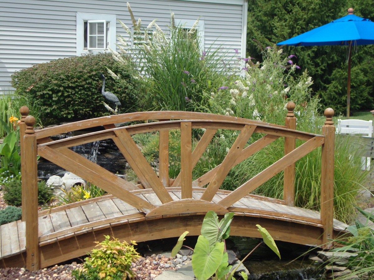 A wooden bridge over a garden pond, surrounded by lush plants and greenery.