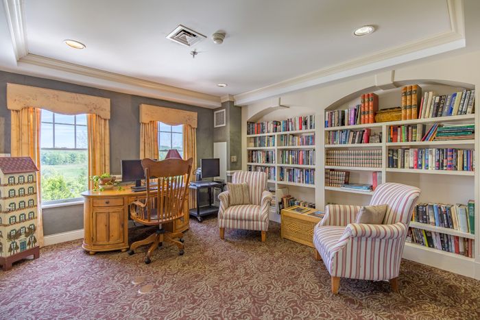 A cozy library with bookshelves, a wooden desk, and comfortable chairs.