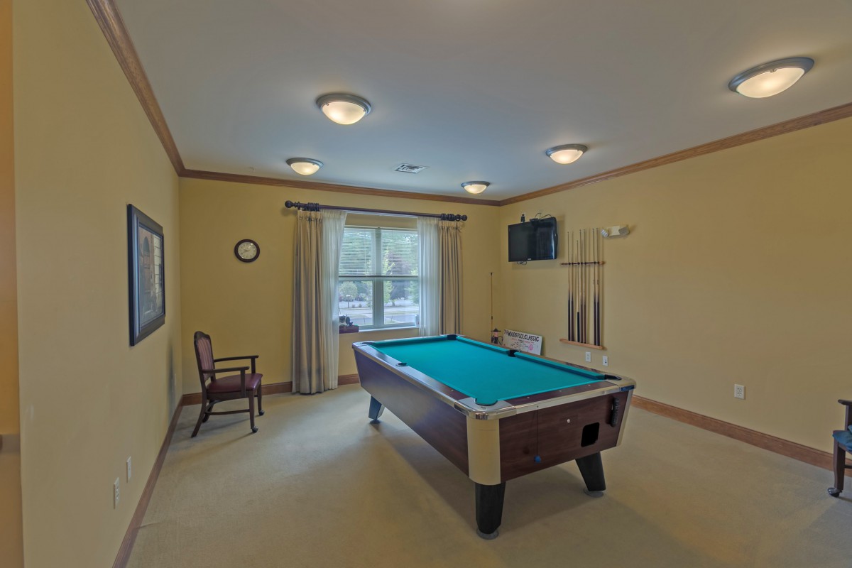 A cozy game room featuring a pool table, television, and seating with natural light from a large window.