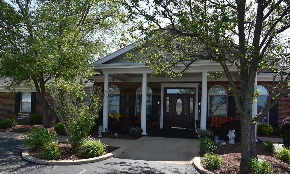 A welcoming building entrance with white columns and surrounding greenery.