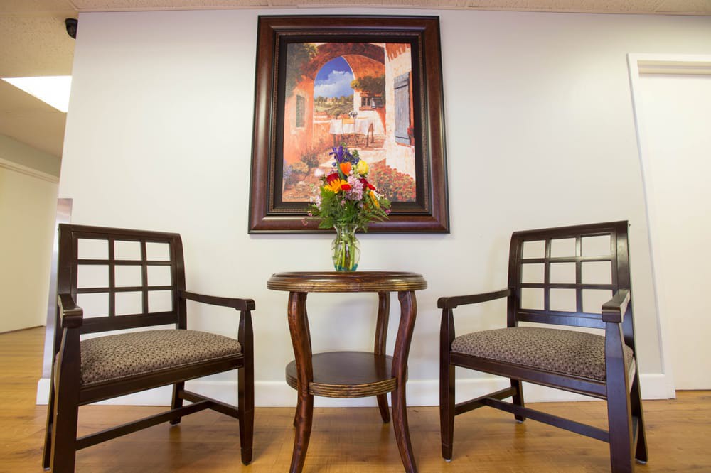 A cozy seating arrangement with two chairs and a small table topped with a vase of flowers, framed by a decorative painting.