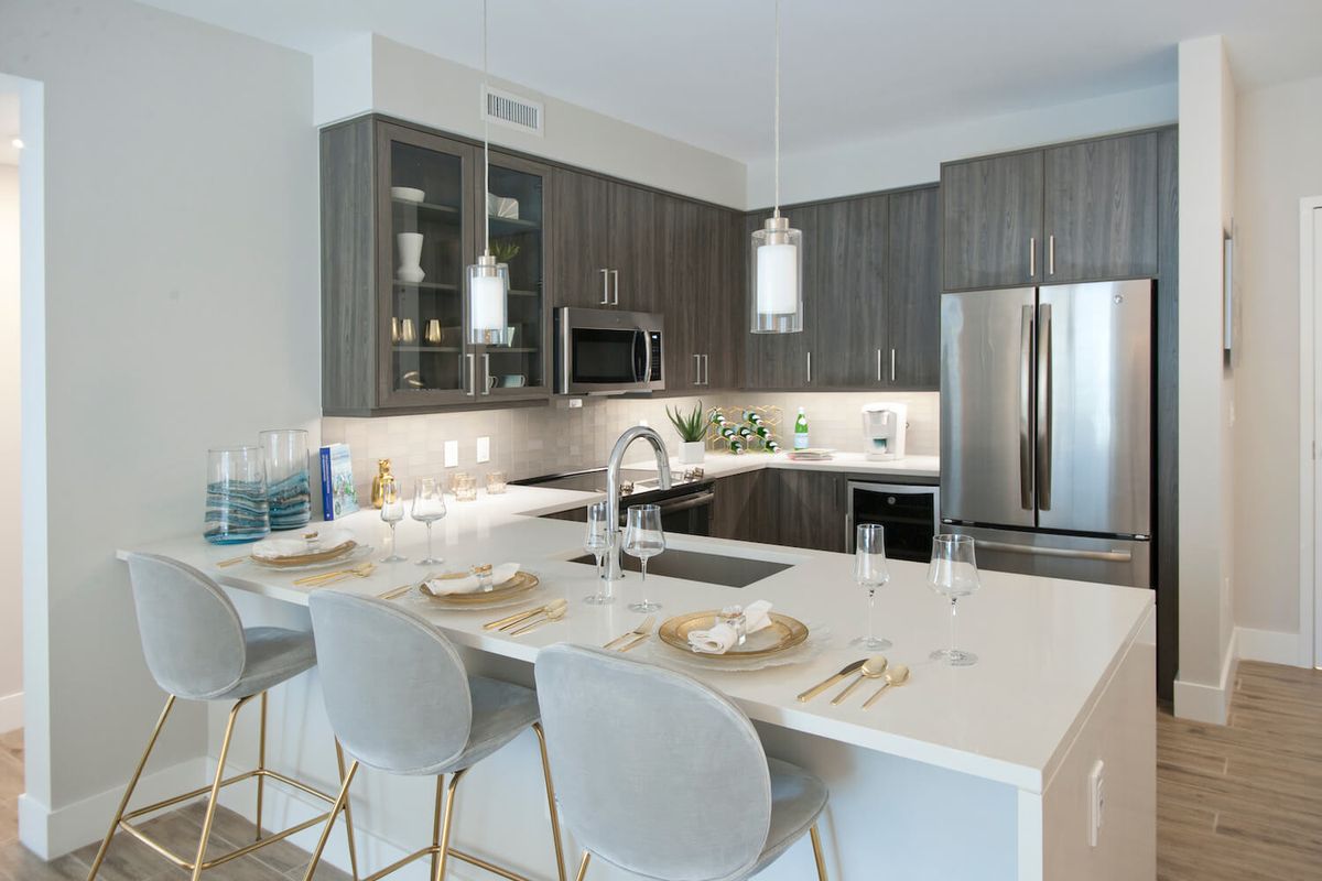 A modern kitchen with sleek cabinetry, an island counter with bar stools, pendant lighting, and stainless steel appliances.