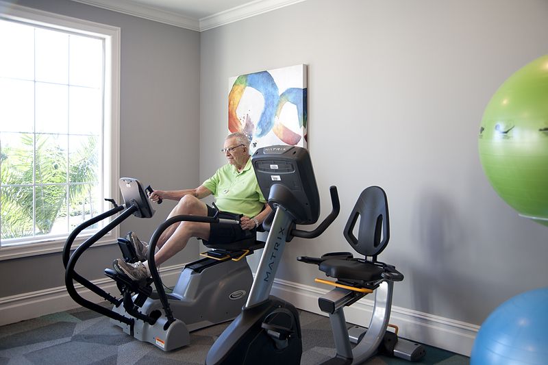 An elderly person exercising on a recumbent bike in a home gym.