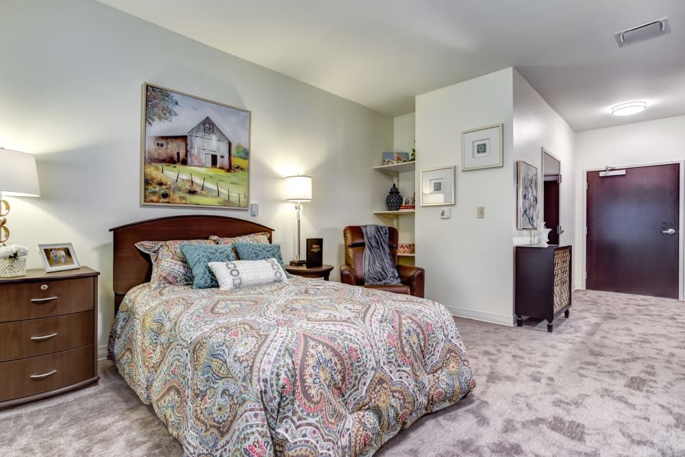 A cozy bedroom with a patterned bedspread, art on the walls, and warm lighting.