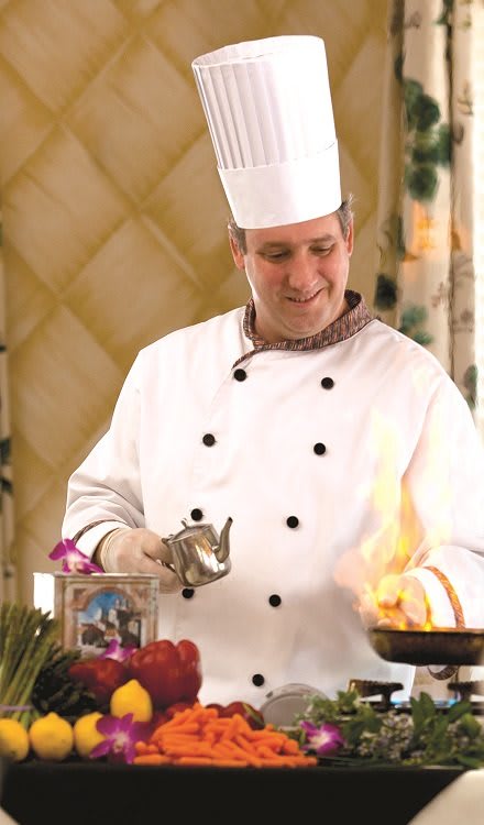 A chef in a white uniform skillfully preparing a dish with flames in the kitchen.