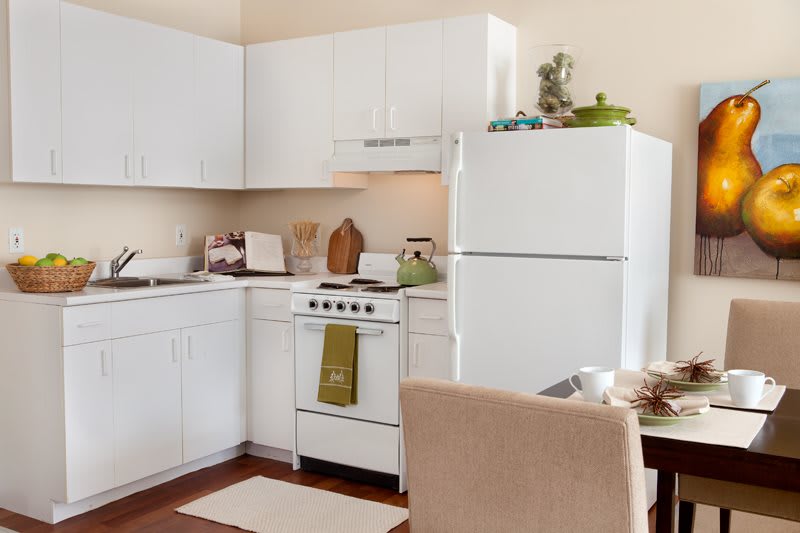 A cozy apartment kitchen with white cabinets, a stove, and a refrigerator.