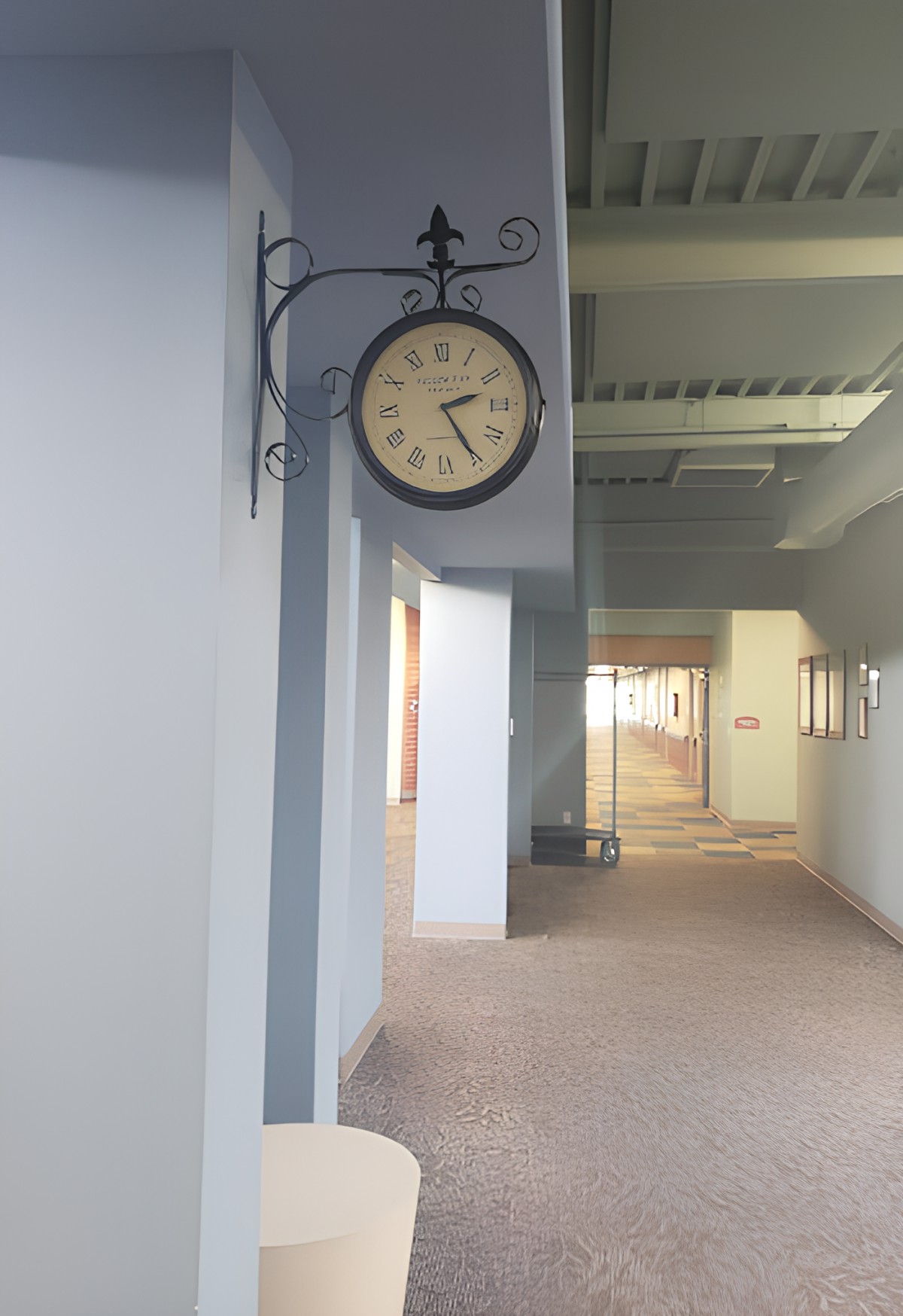 A wall-mounted clock in a bright, empty hallway.