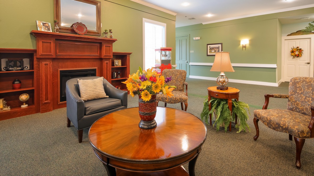A cozy living room with elegant furniture, featuring a wooden table with a vase of flowers, armchairs, and a fireplace creating a warm atmosphere.