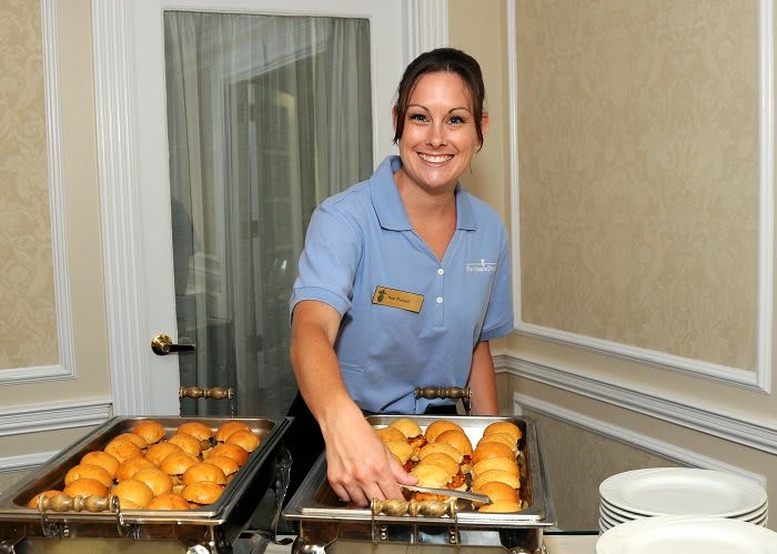 A server in uniform presents a buffet with assorted pastries.