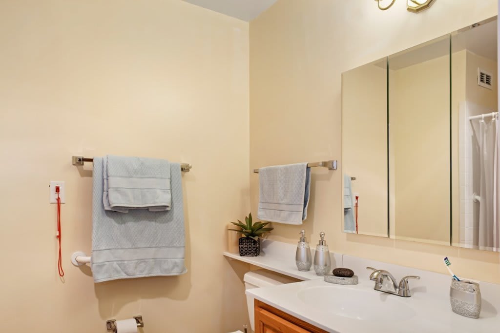 A neatly arranged bathroom with a mirror, sink, and towels hanging on the wall.