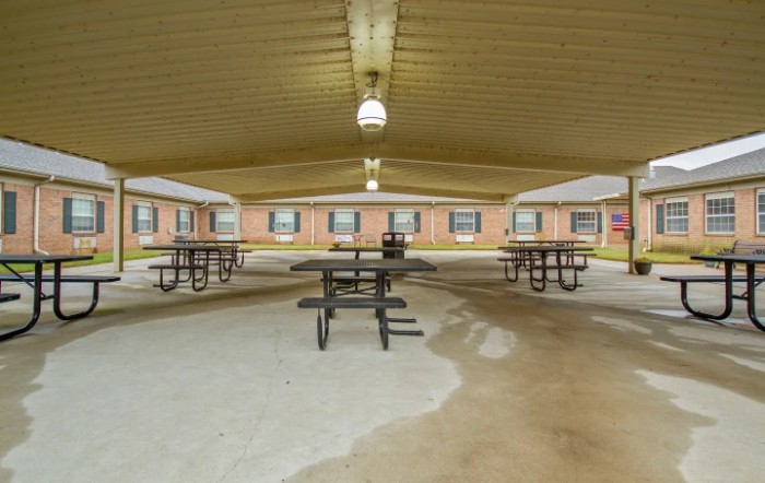 A covered outdoor pavilion with picnic tables surrounded by brick buildings.