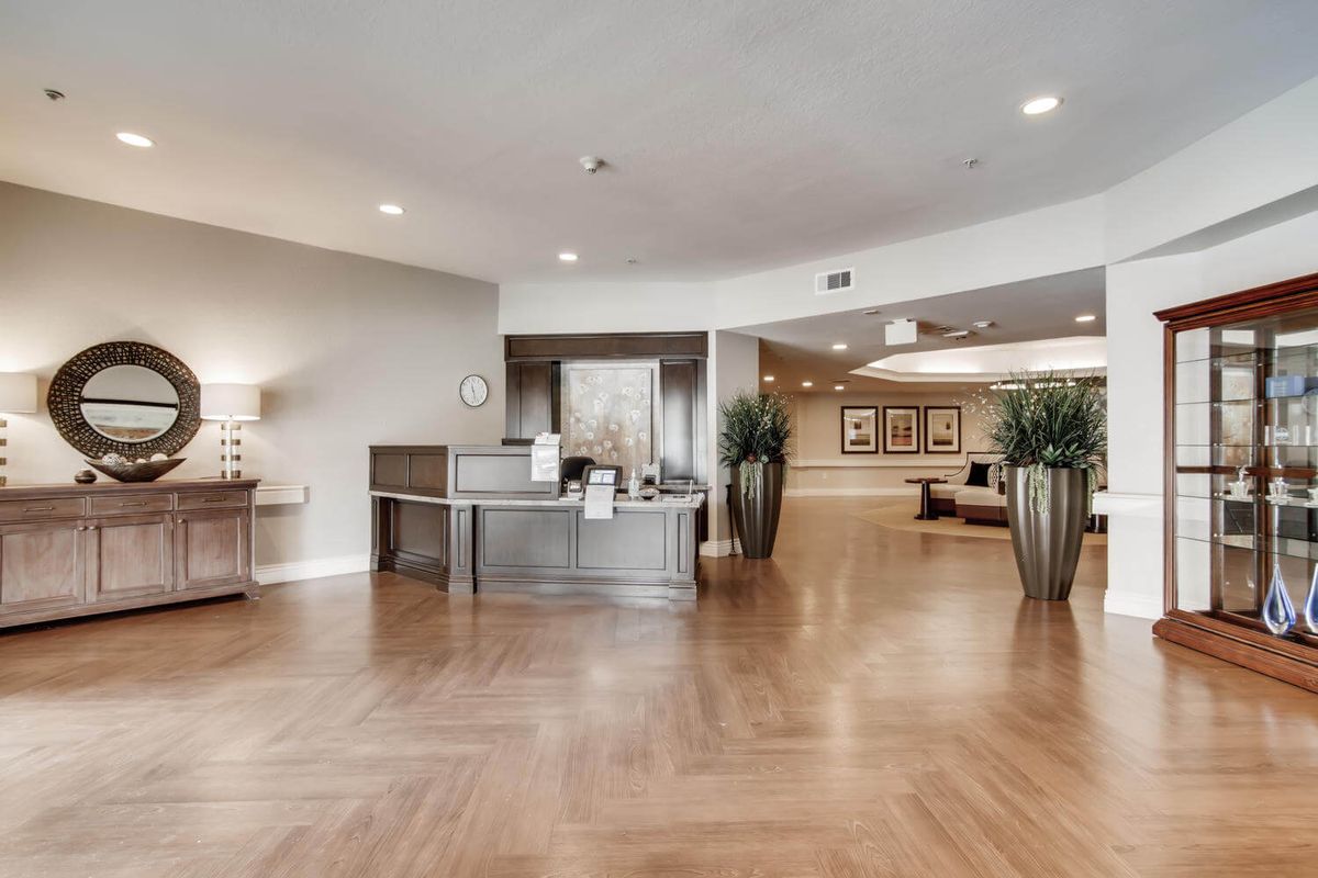 A spacious and modern lobby with wooden flooring, featuring a reception desk and decorative plants.