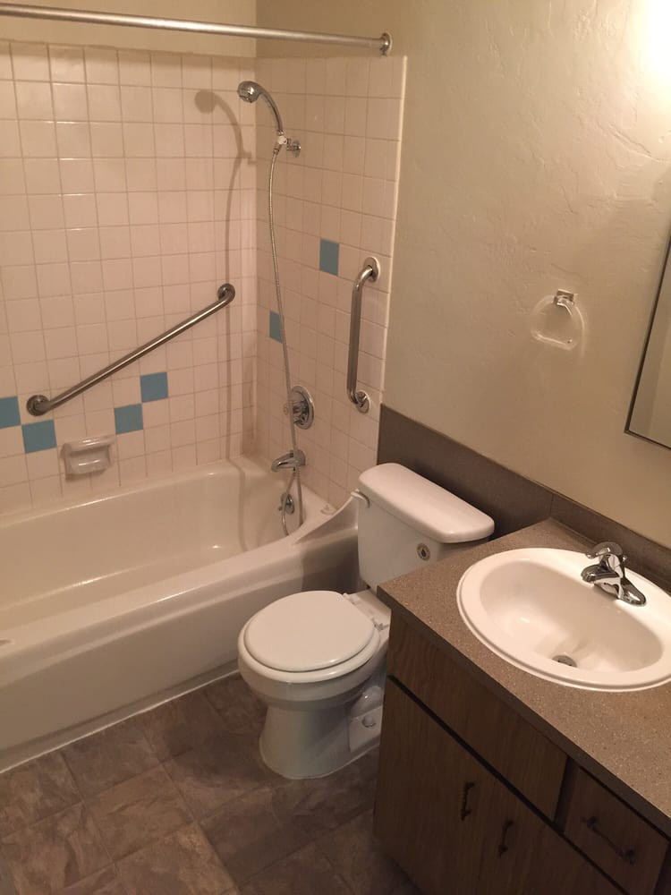 A bathroom with a bathtub, toilet, and sink, featuring grab bars and tiled walls.