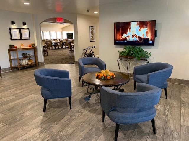 A cozy lobby with blue chairs arranged around a table, featuring a television displaying a virtual fireplace.