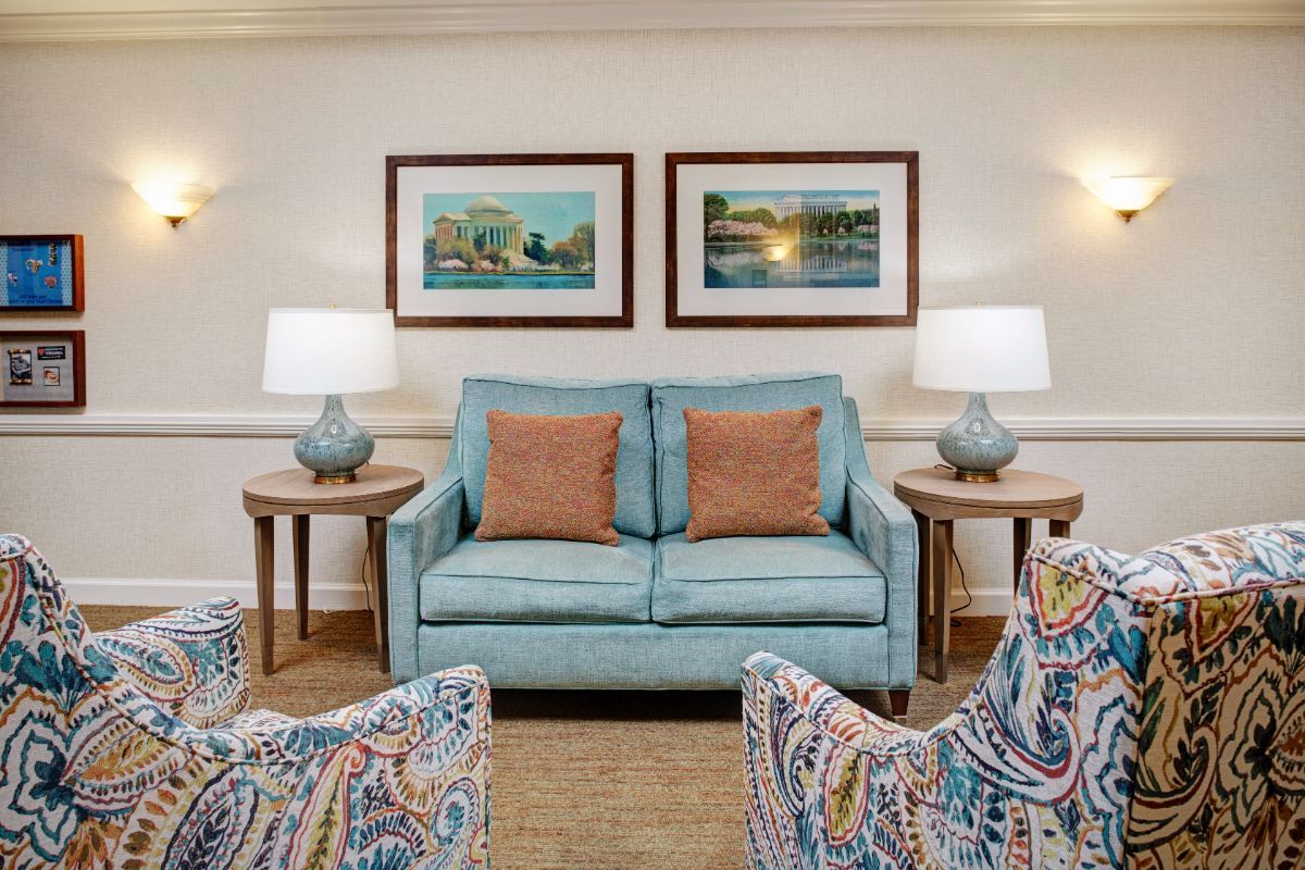 A cozy living room with a blue sofa, patterned chairs, and framed artwork on the wall.