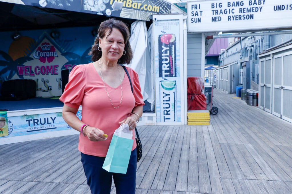 A woman in a peach top holding a shopping bag stands on a boardwalk, with various signs in the background.
