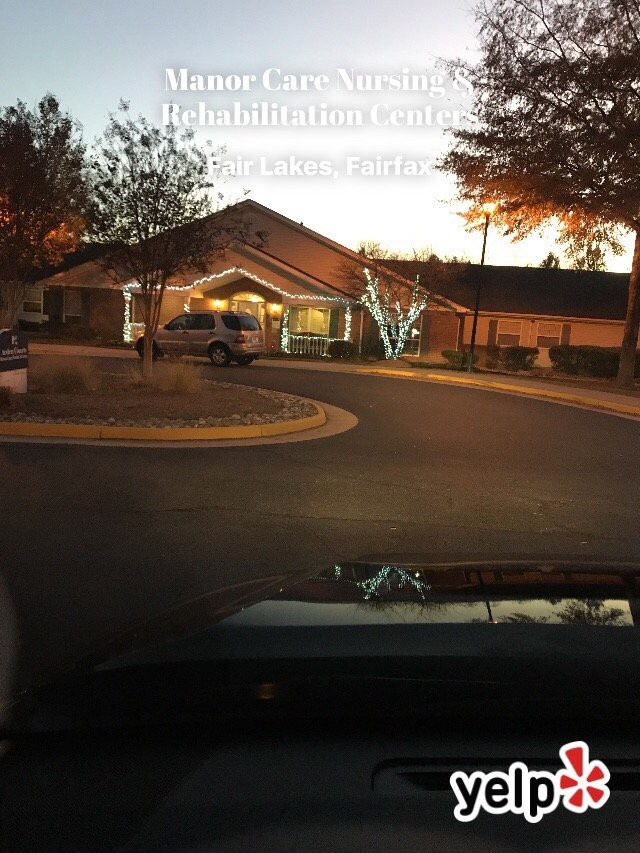 A car approaches a well-lit building entrance during the evening.