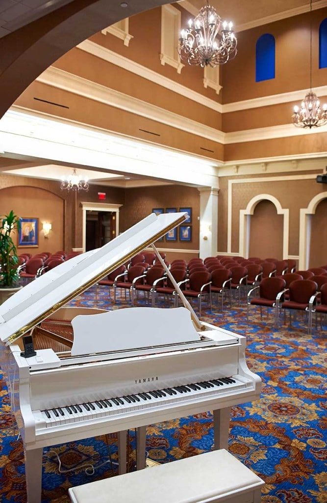 A luxurious lobby interior featuring a white grand piano, elegant seating arrangements, and a decorative chandelier.