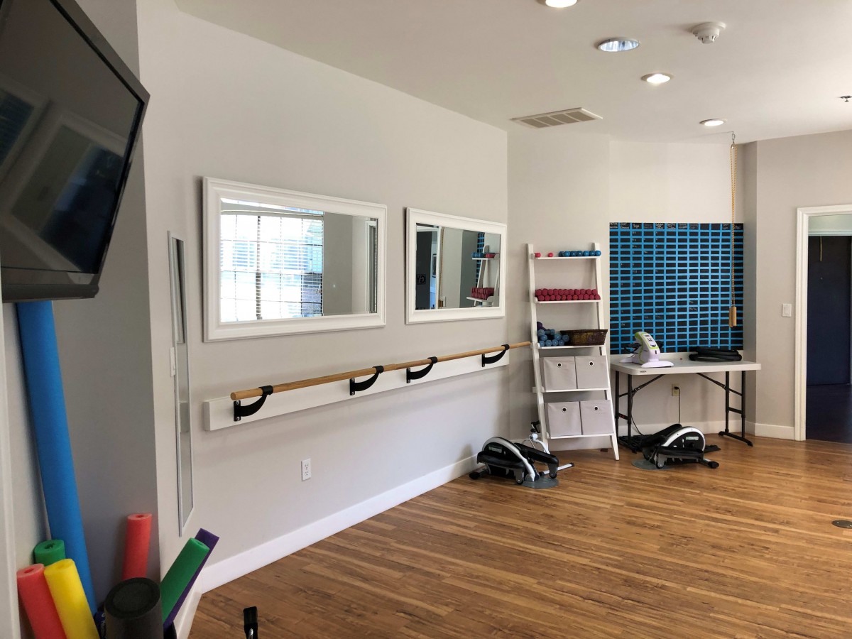A well-lit exercise studio with mirrors, a ballet barre, and fitness equipment.