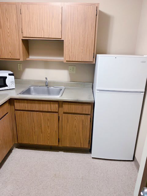A compact kitchen setup with a refrigerator, wooden cabinets, a sink, and a microwave on the countertop.