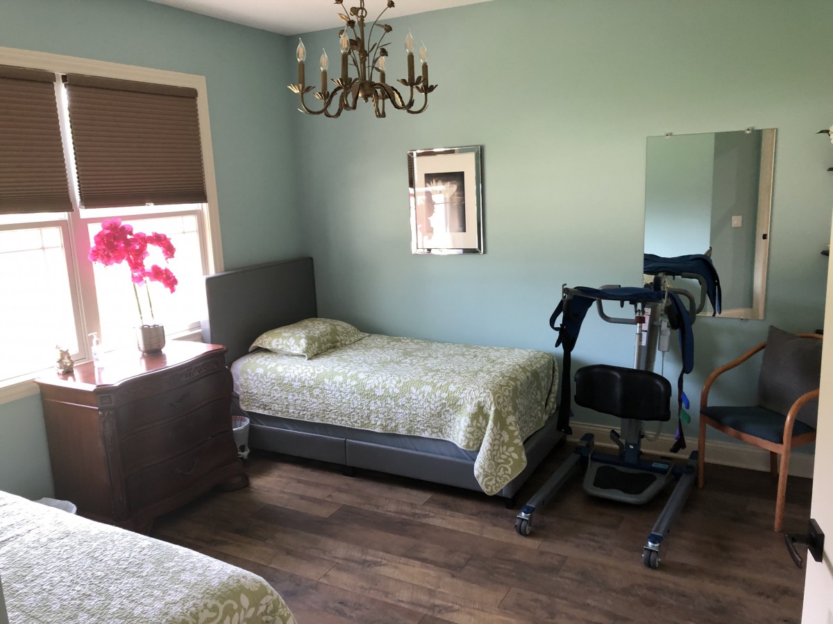A tidy bedroom featuring two single beds, a chandelier, and exercise equipment on a wooden floor.