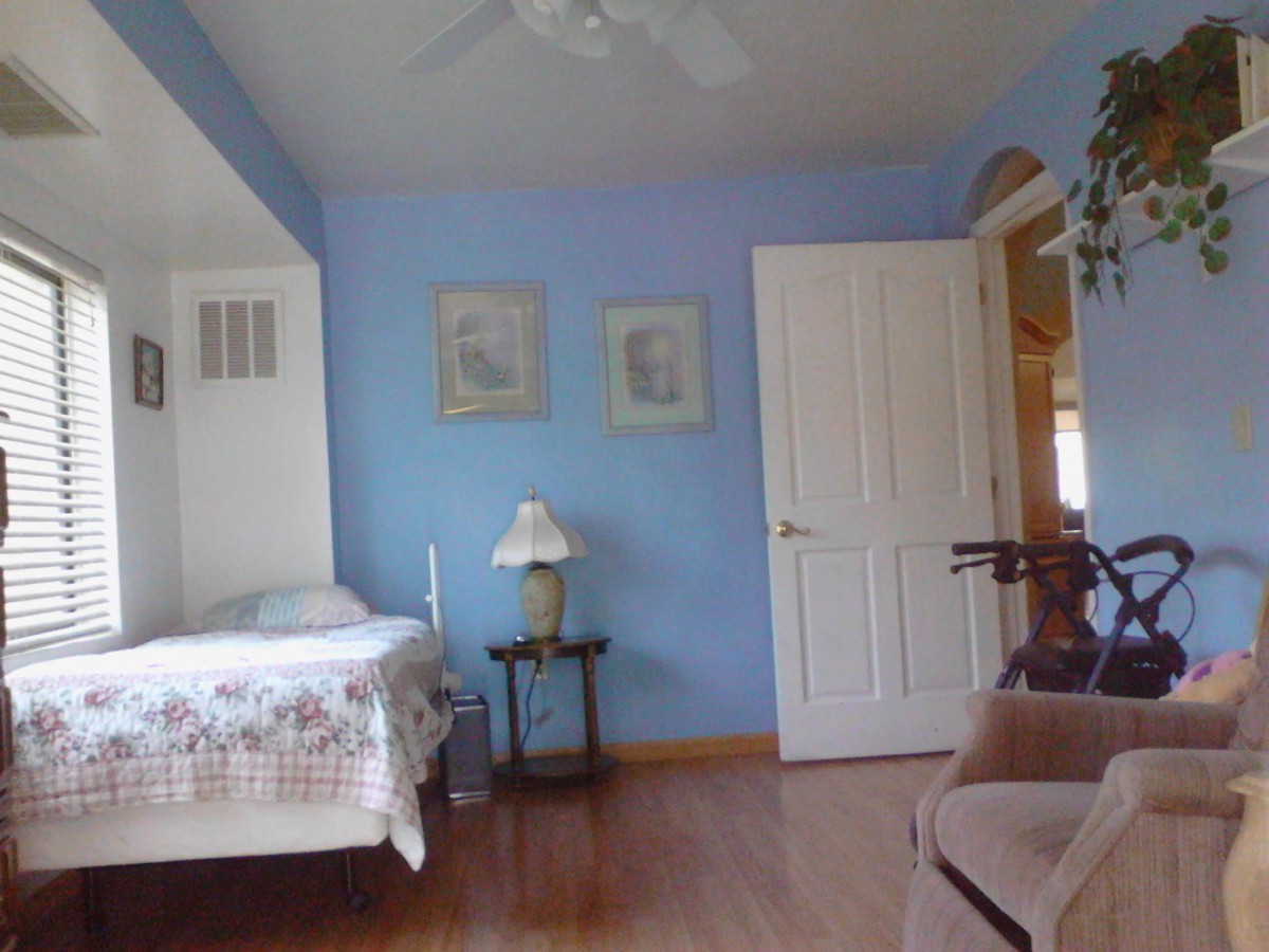 A cozy bedroom with blue walls, featuring a bed and a bedside lamp.