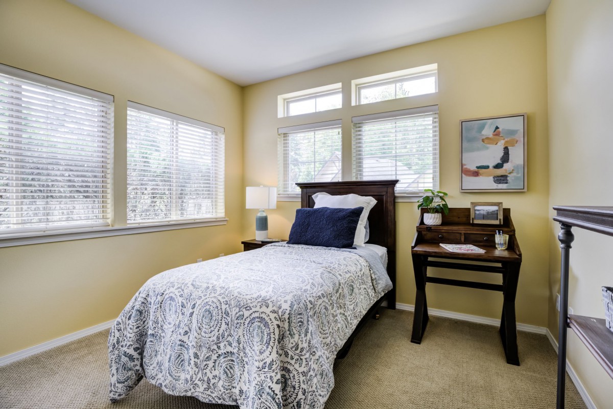 A cozy bedroom with a single bed, a desk, and large windows.