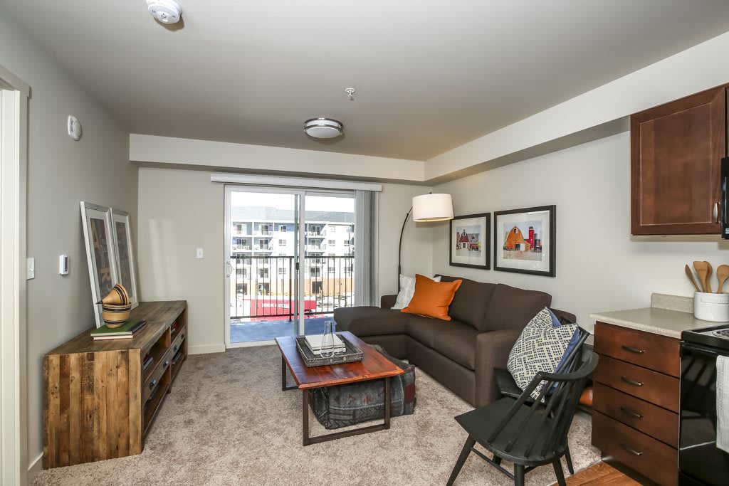 A cozy living room with a comfortable sofa, coffee table, and a television stand. The space is decorated with artwork and has a view of the balcony through sliding glass doors.