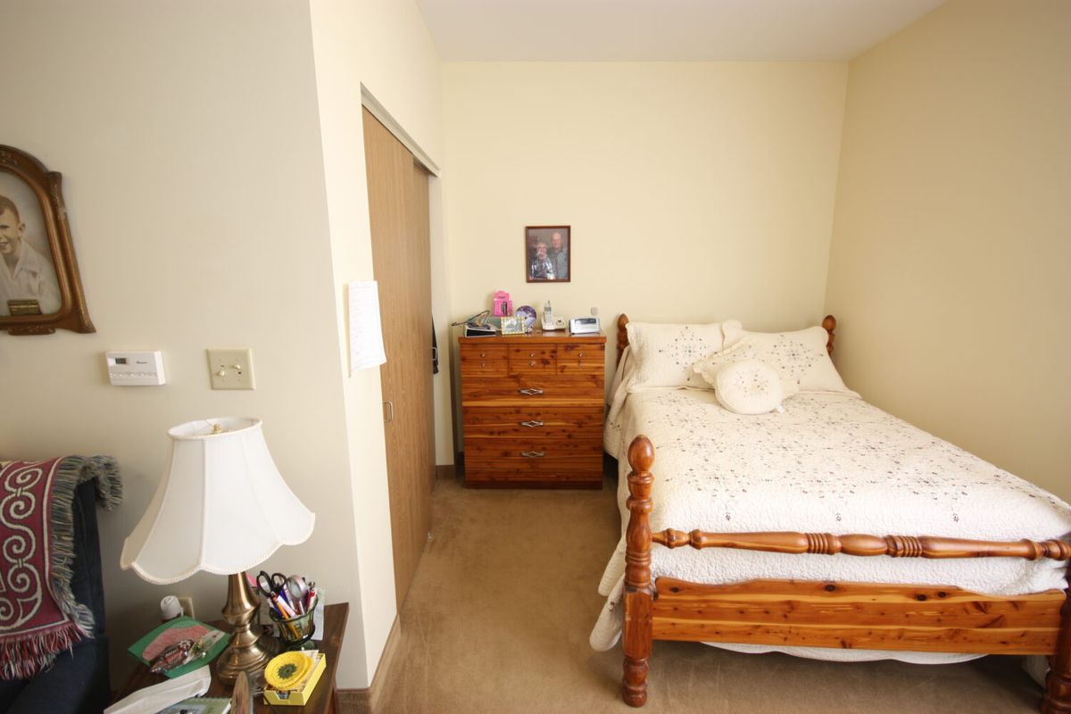 A cozy bedroom with a single wooden bed, a dresser, and a bedside lamp.