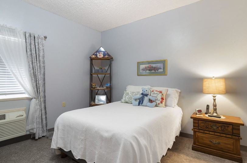 A cozy bedroom with a neatly made bed, nightstand, and soft lighting.