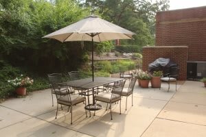 A patio with a table, chairs, and an umbrella set up in a garden area.