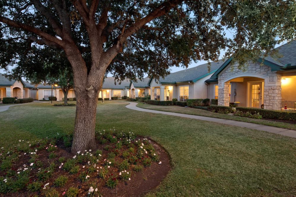A spacious house with a well-maintained garden and large tree in the foreground during the evening.