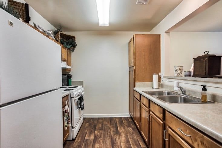 A compact kitchen with wooden cabinets, appliances, and a double sink.