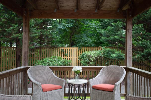 A cozy patio with wicker chairs and a small table overlooking a lush garden.