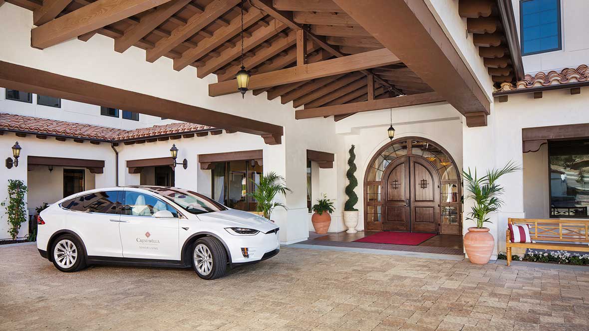 A luxury car parked in front of an elegant building entrance with a wooden door and a covered driveway.