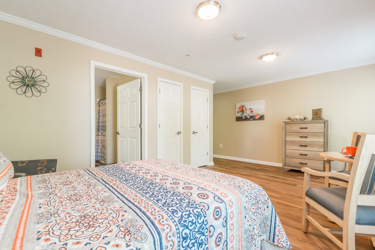A cozy bedroom with a patterned bedspread, dresser, and closet doors.